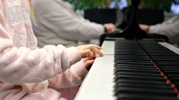 Etualalla lapsen kädet pianon koskettimilla, taustalla näkyy toisen henkilön kädet toisen pianon koskettimilla.