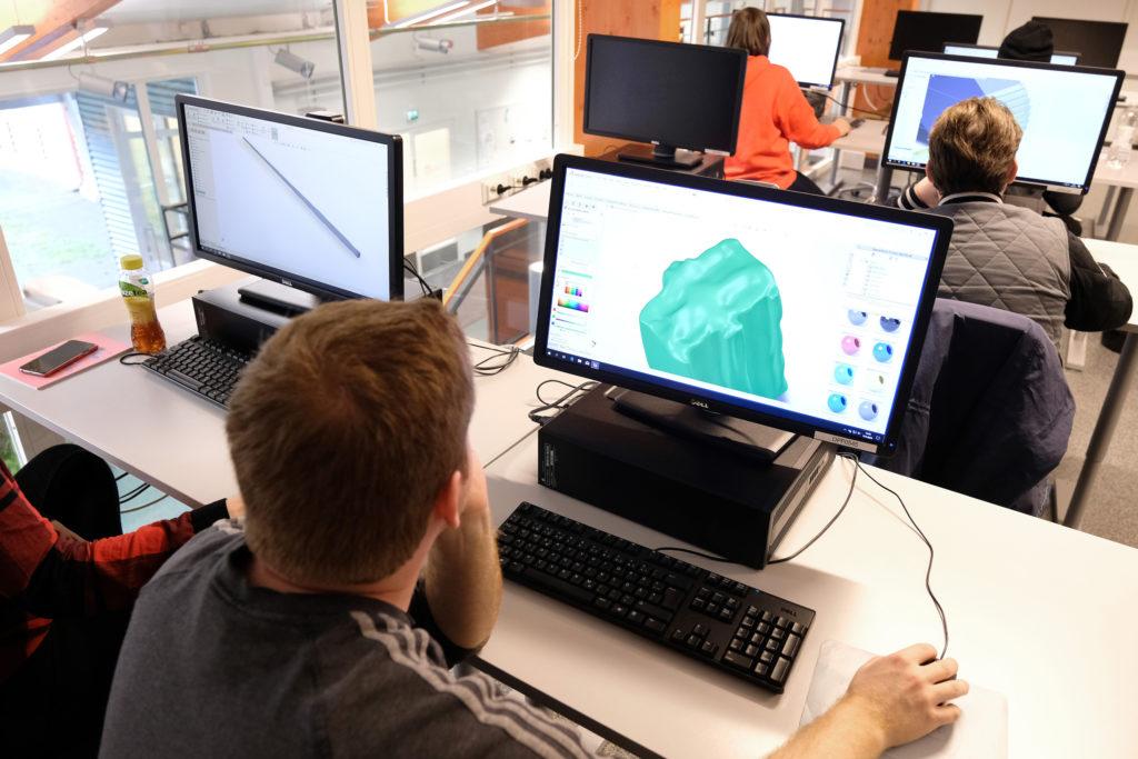 Ihmisiä tietokoneluokassa, tietkoneen ruudulla näkyy 3D-mallinnusohjelmalla työskentelyä.