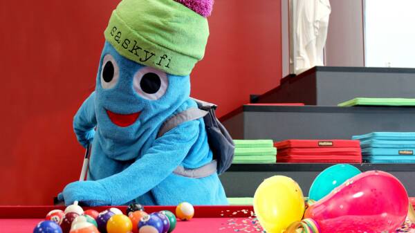 Turkoosi maskottihahmo pelaa biljardia, hahmolla vihreä pipo, jossa pinkki tupsu ja teksti sasky.fi, biljardipöydällä biljardipalloja ja ilmapalloja.