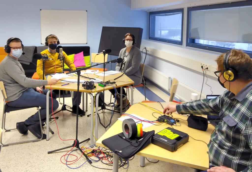 Neljä henkilöä kuulokkeet päässä nauhoittamassa podcastia.