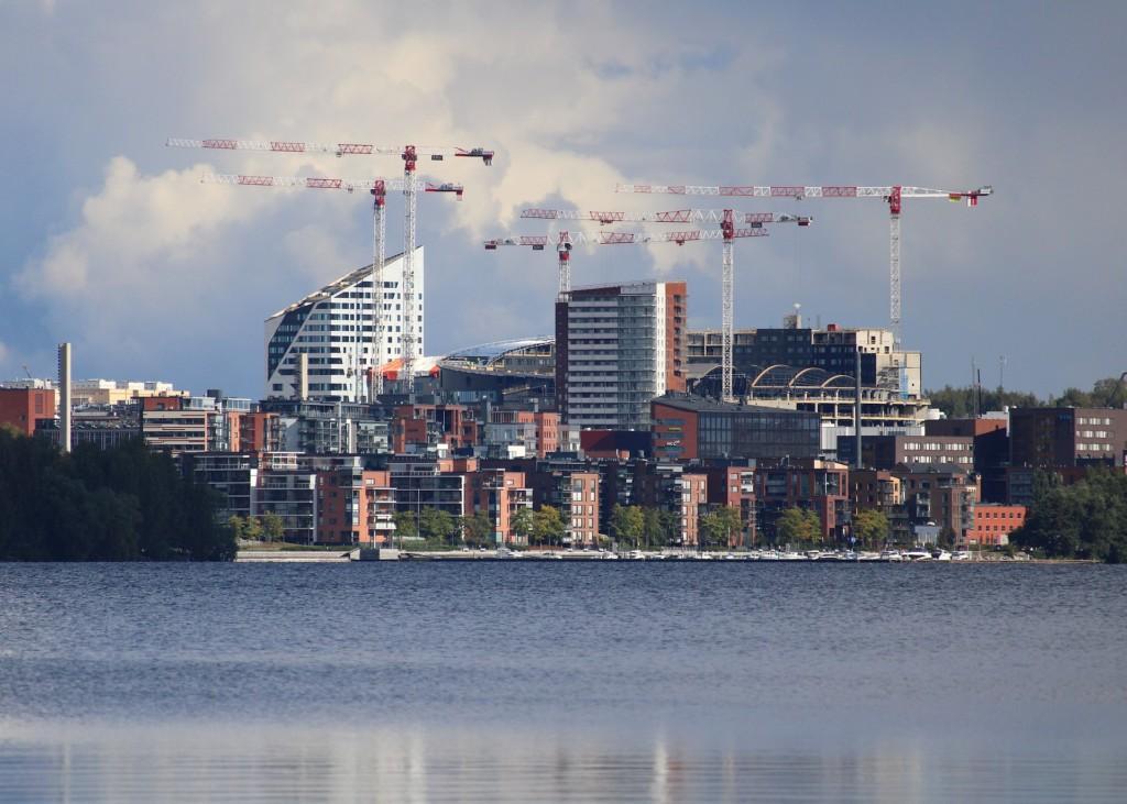 Kuvassa etualalla järvi, jonka takana näkyy kaupunkimaisemaa Tampereelta, uusia ja rakenteilla olevia kerrostaloja, Tampereen Kannen Areena ja rakennustelineitä.