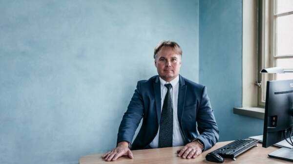 Kuntayhtymäjohtaja Antti Lahti istuu työpöydän takana sinisessä puvussa työhuoneessa, taustalla sininen seinä, pöydällä tietokone ja näppäimistö.