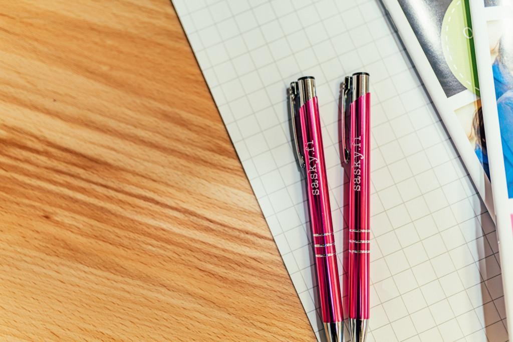 Puisen pöydän päällä ruutupaperia ja kaksi pinkkiä kynää sasky-tekstillä.