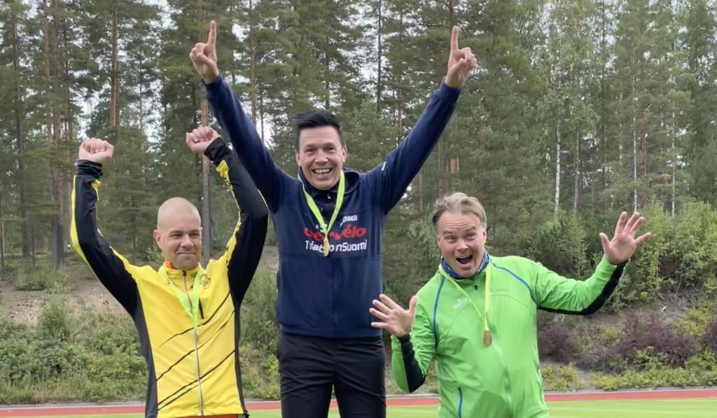 Kolme mieshenkilöä tuulettaa iloisesti mitalit kaulassa.