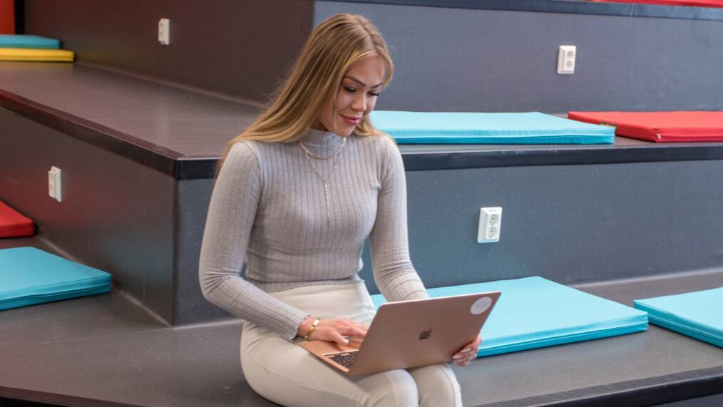 Nuori nainen istuu portailla kannettava tietokone sylissään.