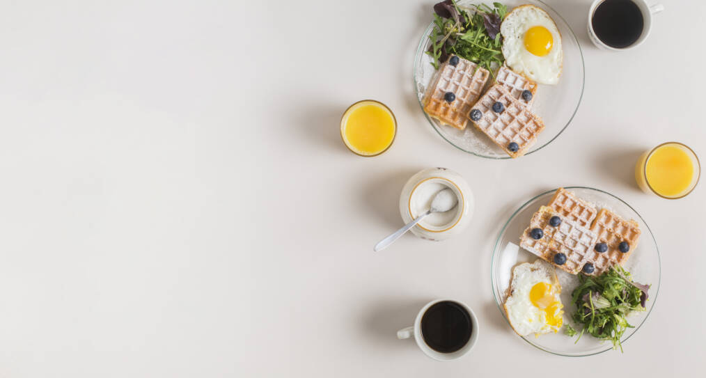 Aamupalapöytä, jossa on kahvia, mehua, vohveleita ja kananmunaa
