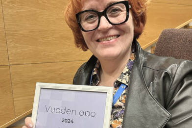 Hymyilevä, silmälasipäinen nainen kädessään kunniakirja, jossa teksti Vuoden opo 2024.