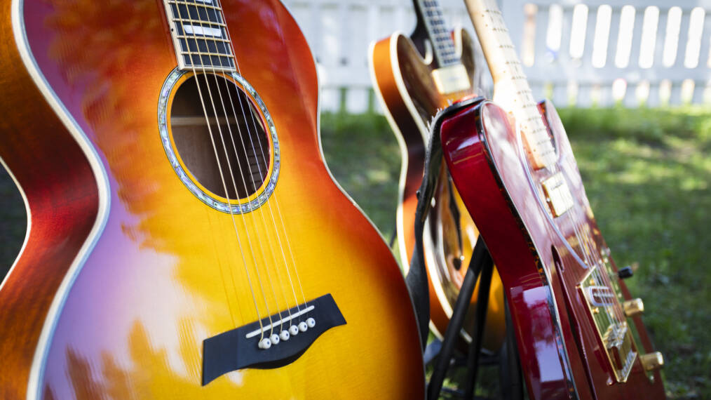 Kuvassa kolme kitaraa. Etualalla on akustinen puna-keltainen kitara lähikuvassa. Taustalla kaksi muuta sähkökitaraa
