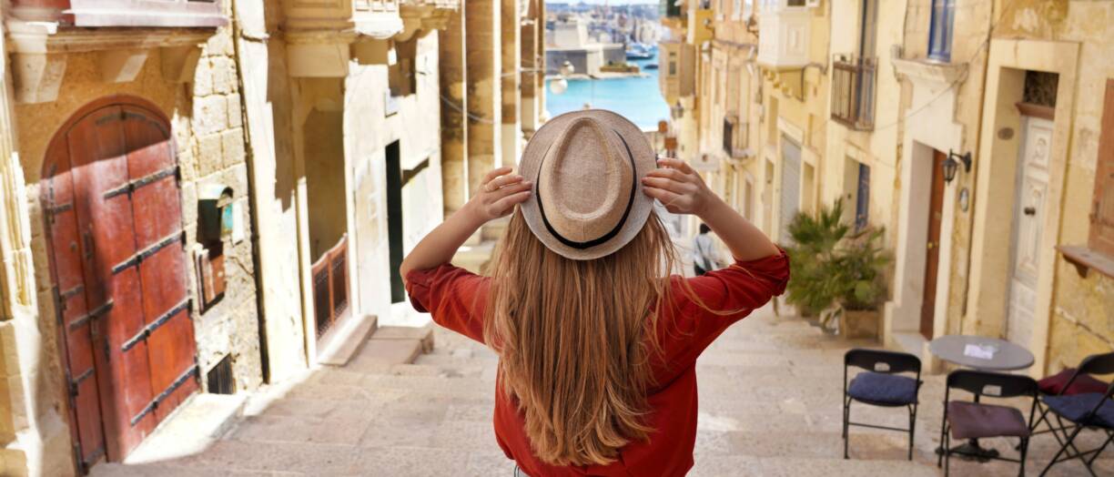 kuva takaa turistista, jolla on hattu ja pitkät hiukset. Henkilö laskeutuu portaita Vallettan vanhassakaupungissa, Unescon maailmanperintökohteessa, Maltalla.