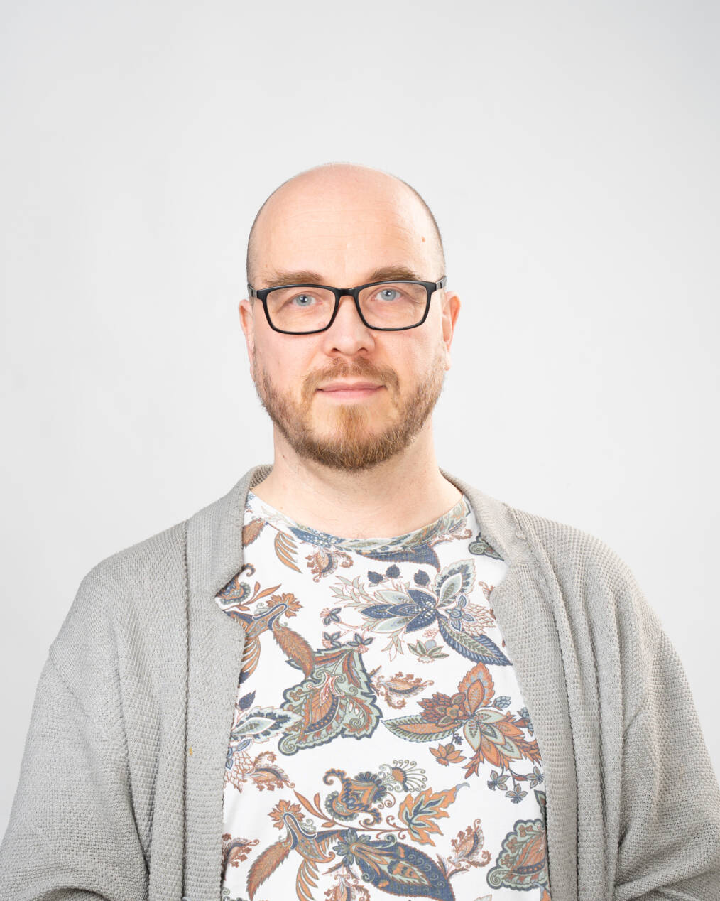 Kuvassa henkilö, jolla kalju päälaki ja silmälasit. Henkilöllä on kukkakuvioinen pusero ja harmaa neuletakki.