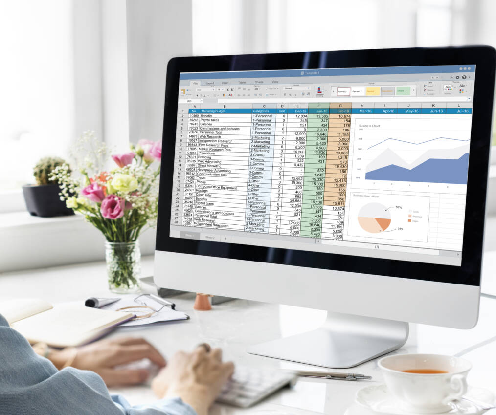 Henkilö työskentelee Excel-taulukon ja kaavioiden parissa tietokoneen ääressä valoisassa työtilassa.
