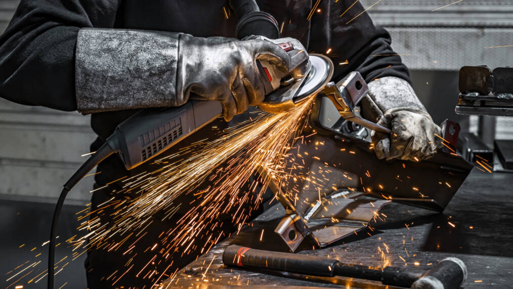 Hitsaaja työskentelee hiomakoneella tulityökorttikoulutuksessa, kipinöitä sinkoaa metallista