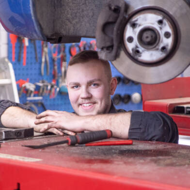 Autonasentaja työssään korjaamolla auton nosturin alla.