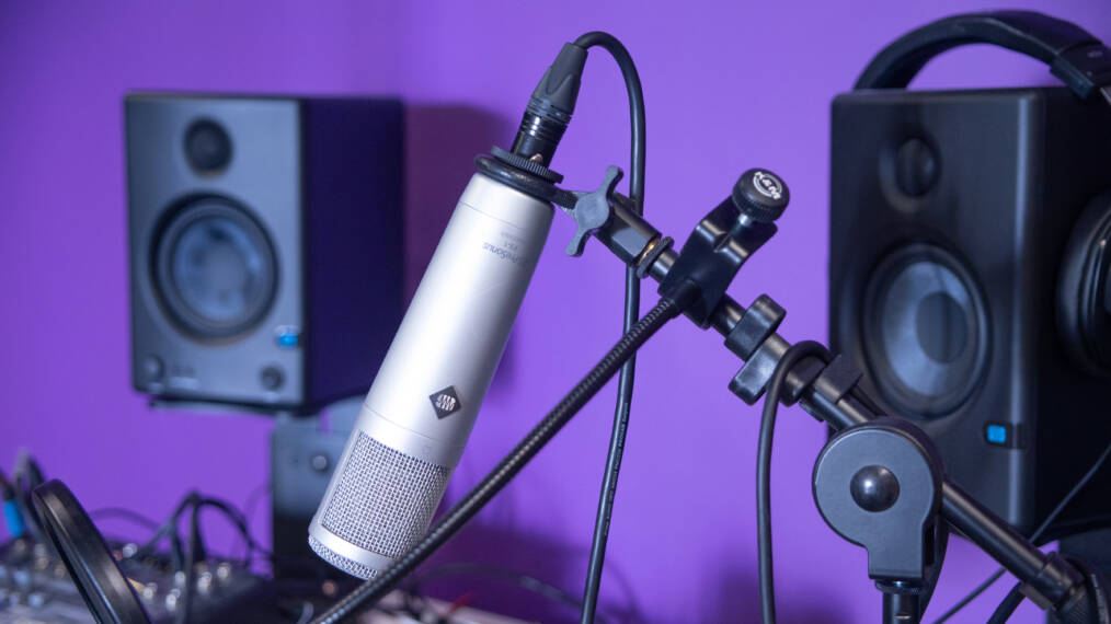 Studioympäristön mikrofoni, kuulokkeet ja kaiuttimet violettia taustaa vasten.
