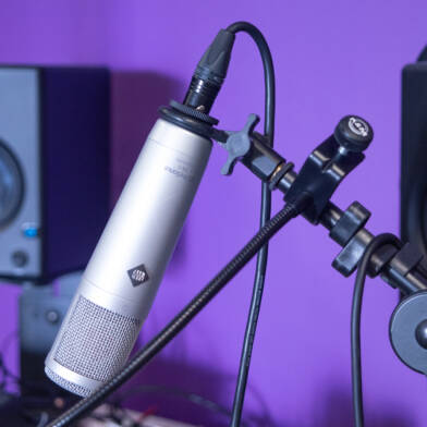 Studioympäristön mikrofoni, kuulokkeet ja kaiuttimet violettia taustaa vasten.