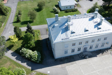 Ilmakuva vaaleasta puurakennuksesta, jossa harmaa konesaumattu peltikatto.