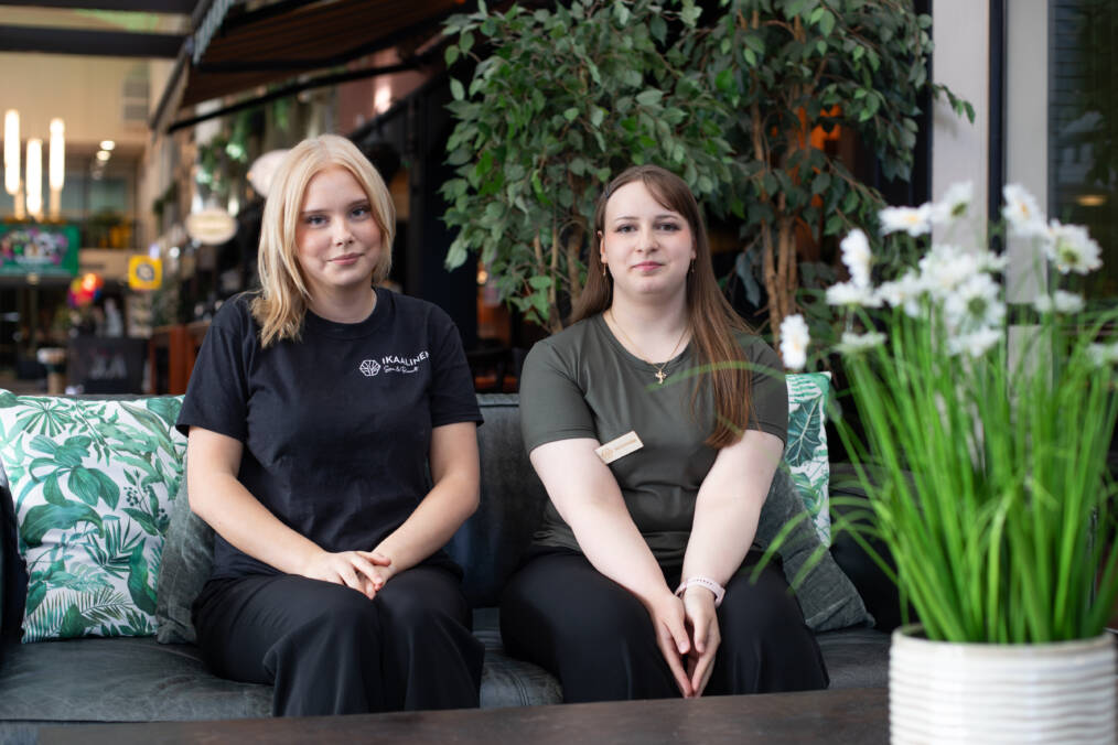 Kaksi henkilöä istuu vierekkäin sohvalla, taustalla näkyy kylpylä-hotellin aulatilaa.