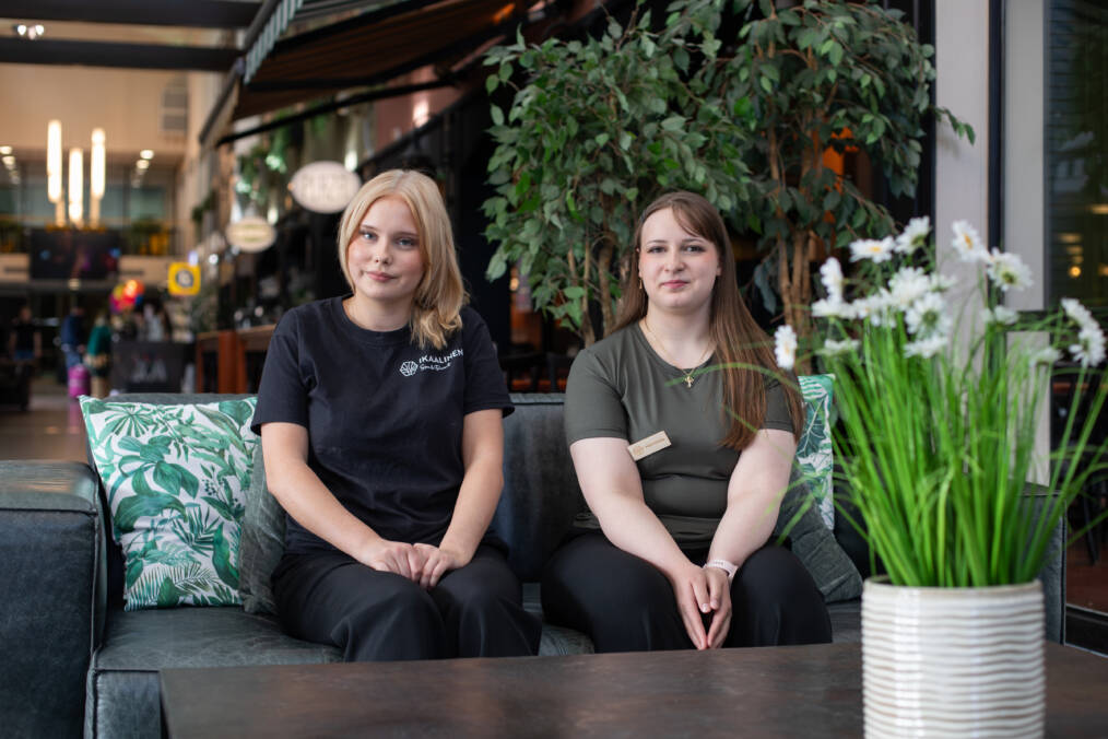 Kaksi henkilöä istuu vierekkäin sohvalla, taustalla näkyy kylpylä-hotellin aulatilaa.