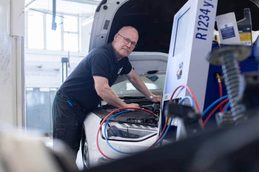 Opettaja työskentelee auton moottoritilassa autokorjaamossa.
