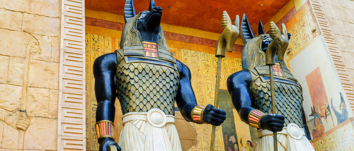 Kaksi historiallista patsasta, jotka esittävät egyptiläistyylisiä taruolentoja, taustalla seinä, jossa hieroklyfikirjoitusta.