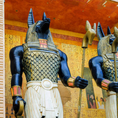 Kaksi historiallista patsasta, jotka esittävät egyptiläistyylisiä taruolentoja, taustalla seinä, jossa hieroklyfikirjoitusta.
