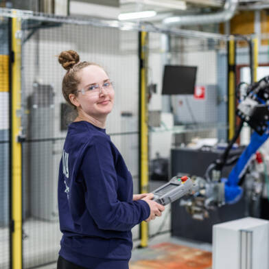 Henkilö käyttää koneistushallissa robottia.