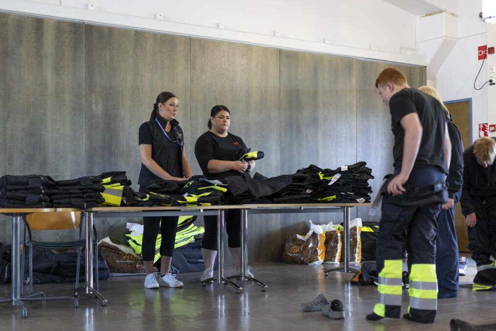 Image Wearin työntekijät ohjaavat opiskelijoita työvaatesovituksessa pöytien ollessa täynnä erikokoisia takkeja ja housuja.