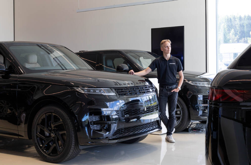 Nuori henkilö seisoo AutoCenterin autohallissa tumman Range Roverin vieressä.