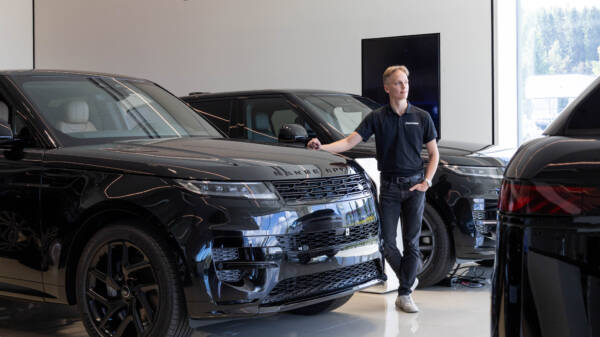 Nuori henkilö seisoo AutoCenterin autohallissa tumman Range Roverin vieressä.