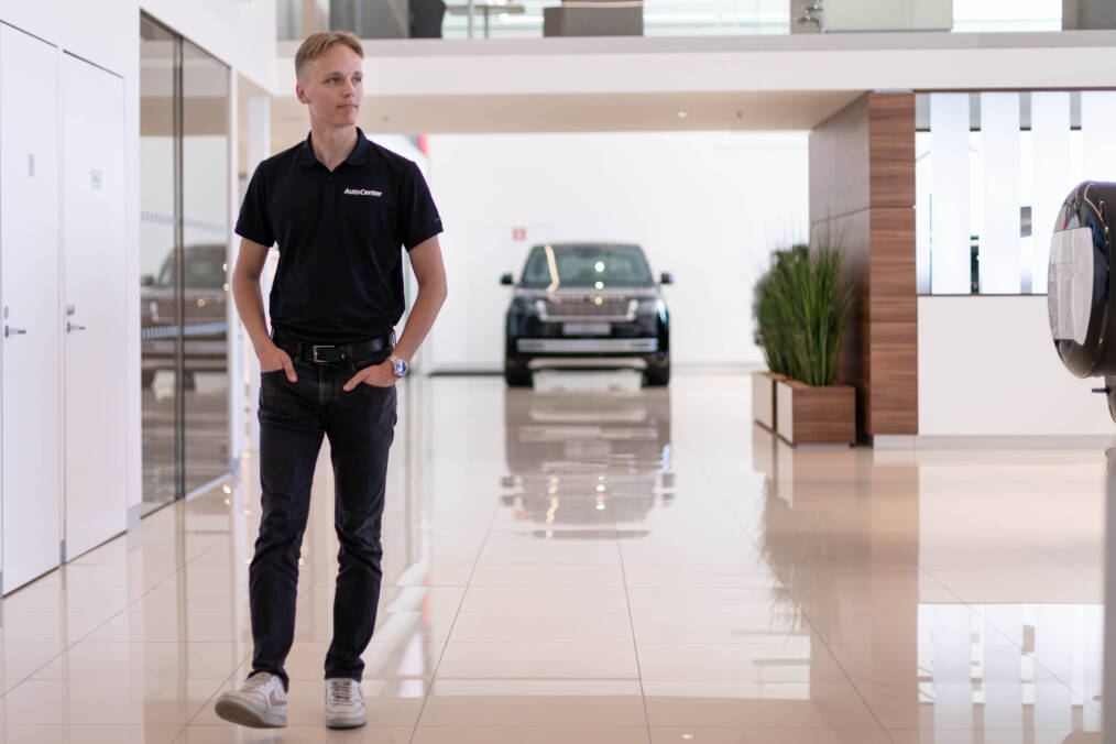 Nuori henkilö kävelee AutoCenterin valoisassa liiketilassa, jossa näkyy taustalla Range Rover.