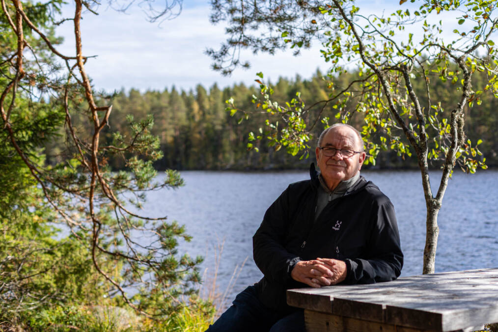 Hannu Raitio istuu järven rannalla pöydän ääressä metsämaisemassa.